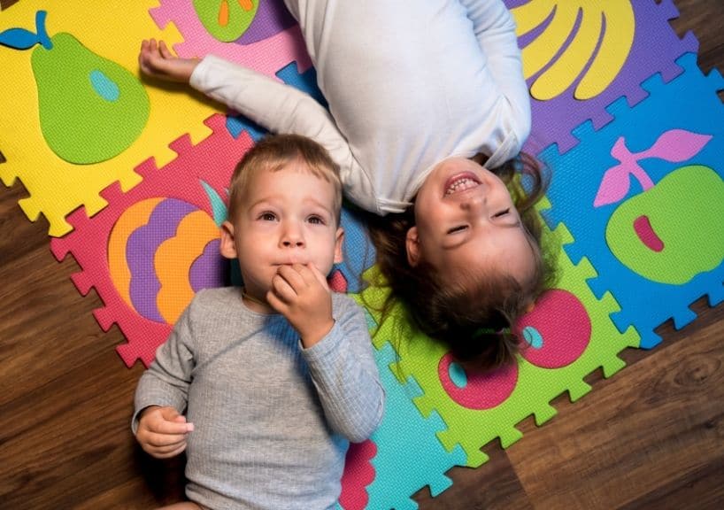 Colorful children playing on foam puzzle mats with abstract fruit designs, promoting childhood development and therapy.