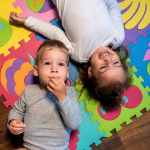 Colorful children playing on foam puzzle mats with abstract fruit designs, promoting childhood development and therapy.